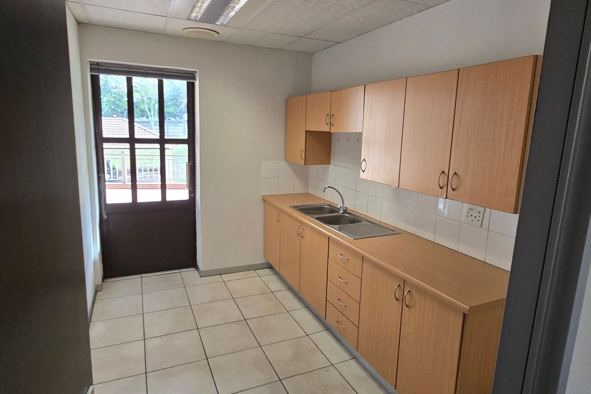 A functional commercial kitchen area featuring laminate cabinetry, a stainless steel double sink, tiled flooring, and direct access to an outdoor space.