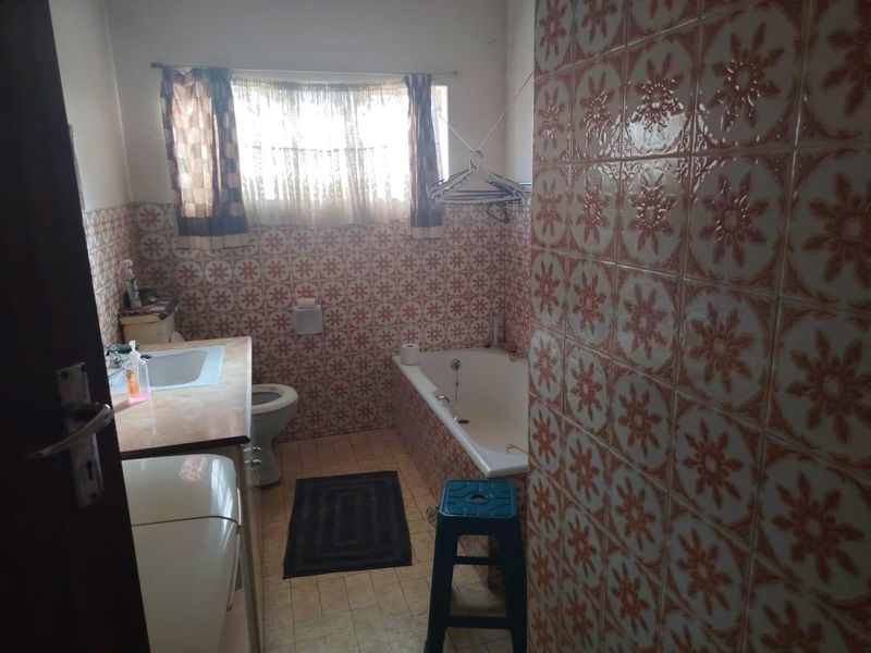A dated bathroom featuring original patterned wall tiles, a built-in vanity with integrated sink, a standard toilet, and a bathtub.