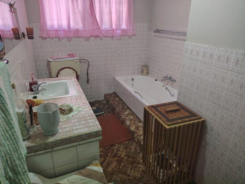 A dated bathroom featuring a built-in tiled vanity, inset basin, and a sunken bathtub with classic wall tiling.