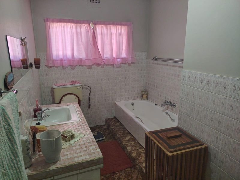 A dated bathroom featuring a built-in vanity with tiled countertop, inset sink, and a built-in bathtub with surrounding wall tiling.