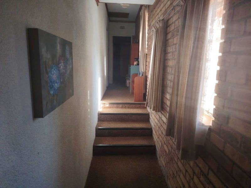 A narrow hallway featuring exposed brick walls and carpeted stairs leading to an upper level, with natural light entering from the side.