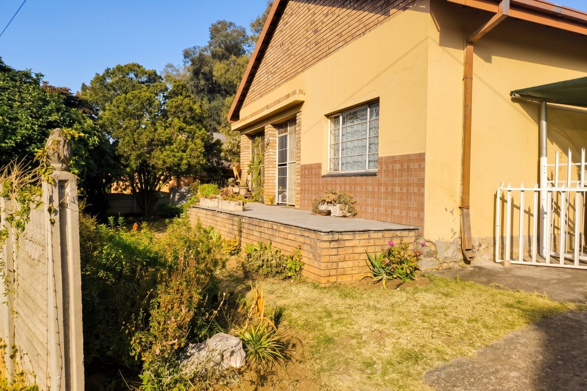 Rear exterior view of the house featuring a raised tiled patio, brick facade, and security features, set within a garden area.