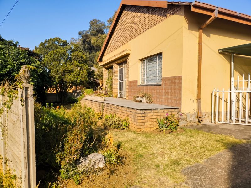 Rear exterior view of the house featuring a raised tiled patio, brick facade, and security features, set within a garden area.