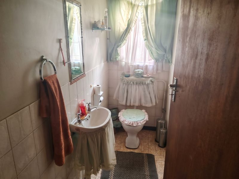A compact bathroom featuring a pedestal basin, toilet, and tiled finishes, offering a functional space with potential for modernization.