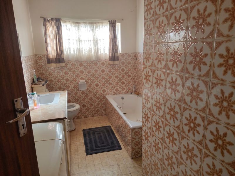 A dated bathroom featuring patterned wall tiles, a built-in bathtub, a vanity basin, and a toilet, offering potential for a modern renovation.