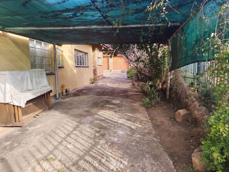 Rear exterior area featuring a concrete driveway, shade cloth canopy structure, and access to a double garage with brick exterior walls.