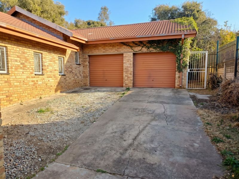 Exterior view of a double garage with a brick facade, tiled roof, and a concrete driveway showing signs of wear and cracking.
