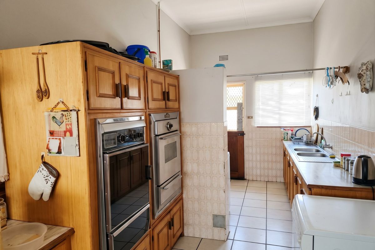 A functional kitchen featuring wooden cabinetry, a built-in double oven, tiled splashbacks, and a double stainless steel sink with tiled flooring throughout.