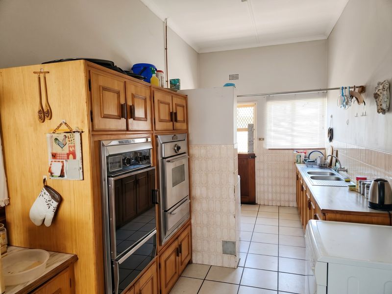 A functional kitchen featuring wooden cabinetry, a built-in double oven, tiled splashbacks, and a double stainless steel sink with tiled flooring throughout.