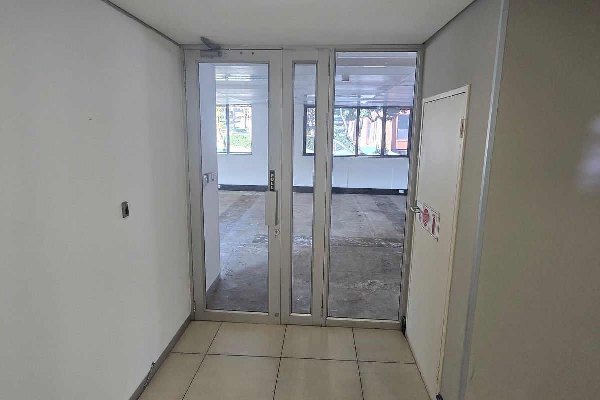 A functional commercial entry area featuring tiled flooring and an aluminium-framed glass door leading into an open-plan office space.