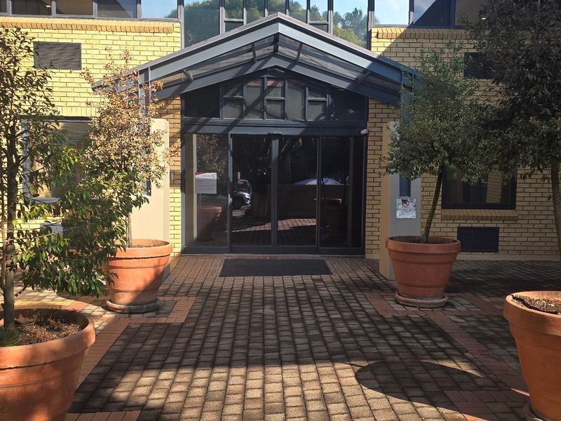 Commercial building entrance featuring a paved courtyard, brick facade, and a modern glass canopy over the main sliding door access.