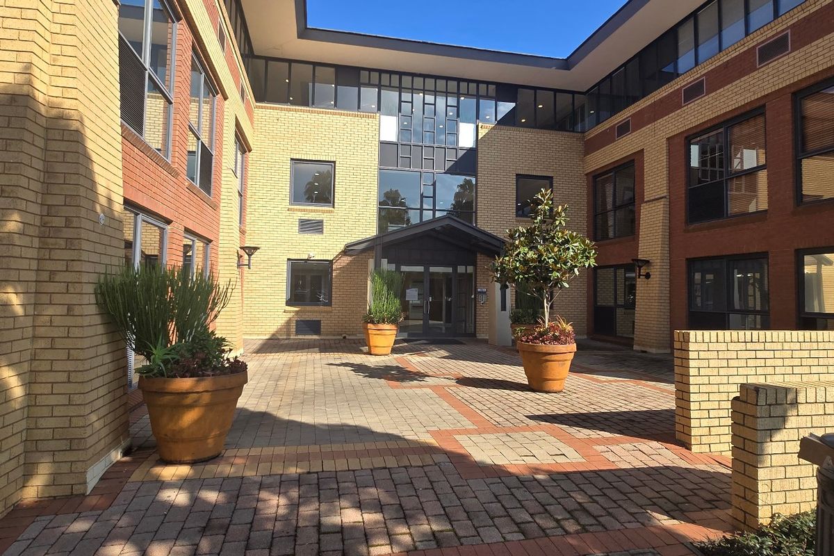 A well-maintained commercial building entrance featuring a paved courtyard, brick facade, and modern glass entry doors.