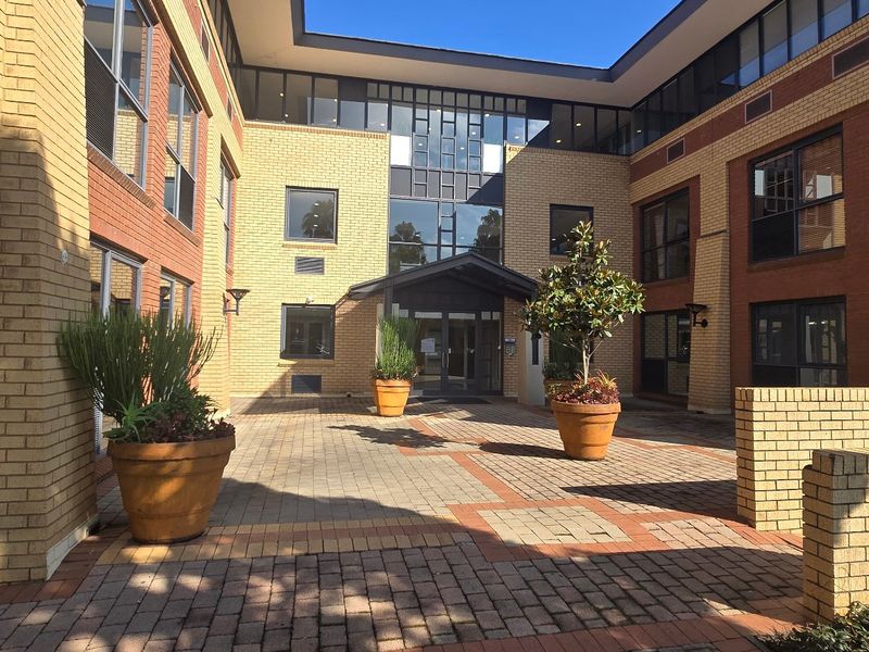 A well-maintained commercial building entrance featuring a paved courtyard, brick facade, and modern glass entry doors.