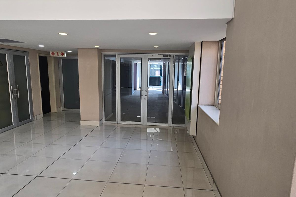 A clean, modern commercial hallway featuring tiled flooring, recessed downlighting, and multiple aluminium-framed glass access doors.