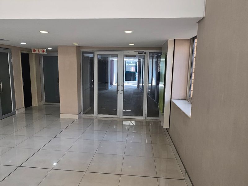 A clean, modern commercial hallway featuring tiled flooring, recessed downlighting, and multiple aluminium-framed glass access doors.