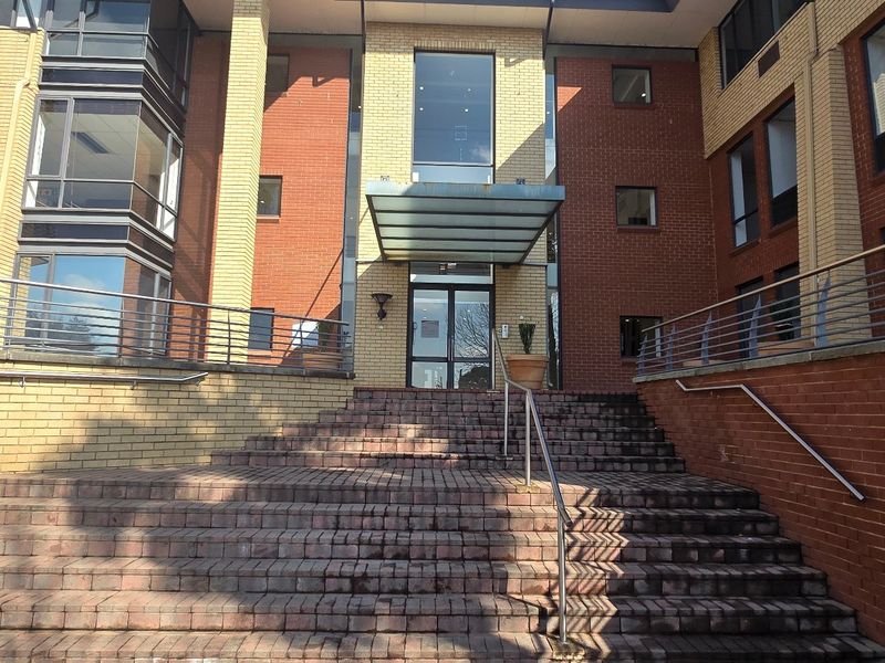Front entrance of a commercial building featuring a brick facade, glass canopy, and a wide brick staircase with metal handrails.