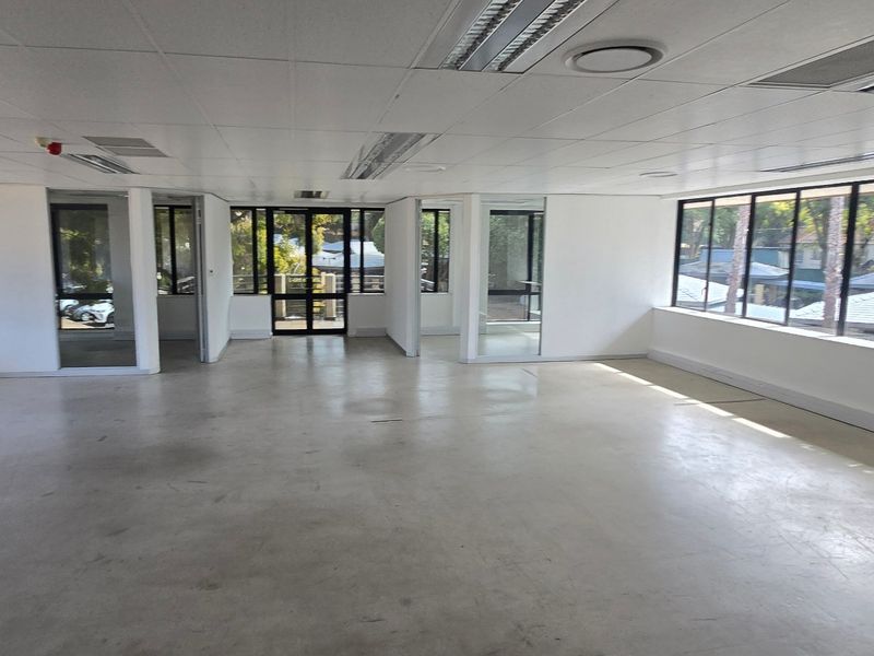 Spacious open-plan commercial office area featuring polished concrete floors, suspended ceilings with recessed lighting, and extensive glass windows providing natural light.