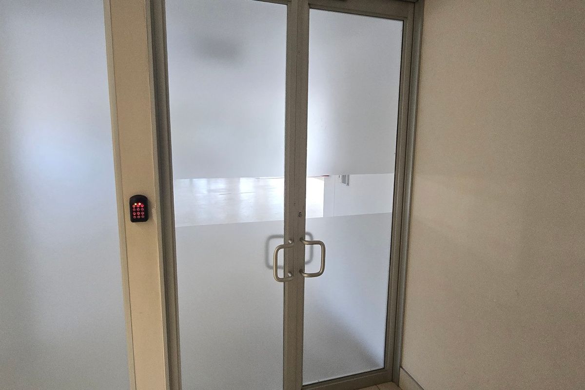 A secure commercial entrance featuring frosted glass double doors with an integrated digital keypad lock and aluminum framing.
