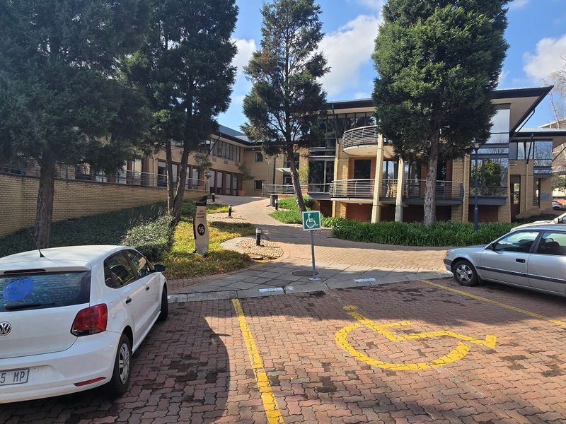 Exterior view of a commercial office complex featuring brick paving, designated disabled parking, and landscaped grounds with multi-level building architecture.