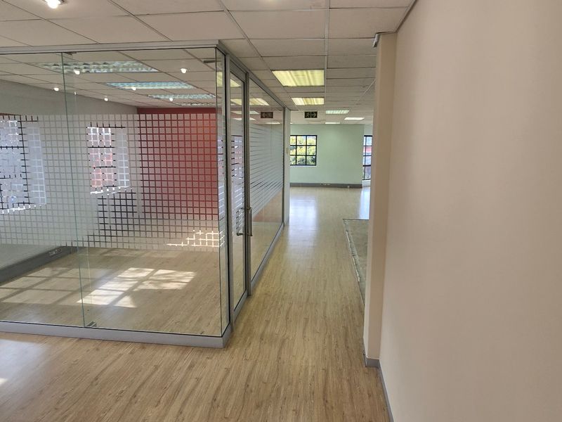 A bright, open-plan commercial office space featuring modern glass partitioning, suspended ceilings with recessed lighting, and durable laminate flooring throughout.