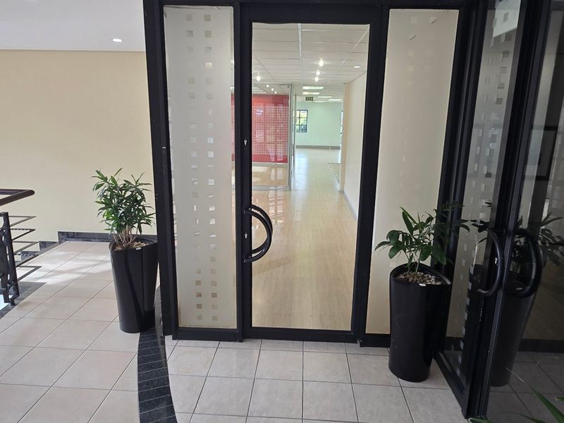 A bright and professional commercial office entrance featuring tiled flooring, a modern glass-panelled door, and a staircase with metal railings.