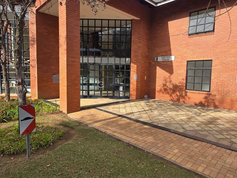 Front exterior view of a commercial office building featuring a red brick facade, glass entrance, and paved walkway.