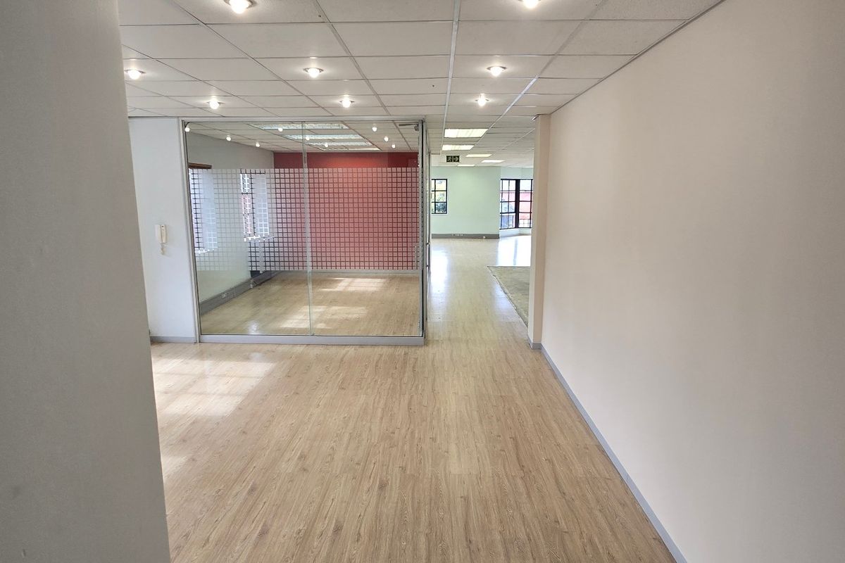 An open-plan commercial office space featuring a glass-partitioned meeting room, suspended ceiling with recessed lighting, and modern laminate flooring.