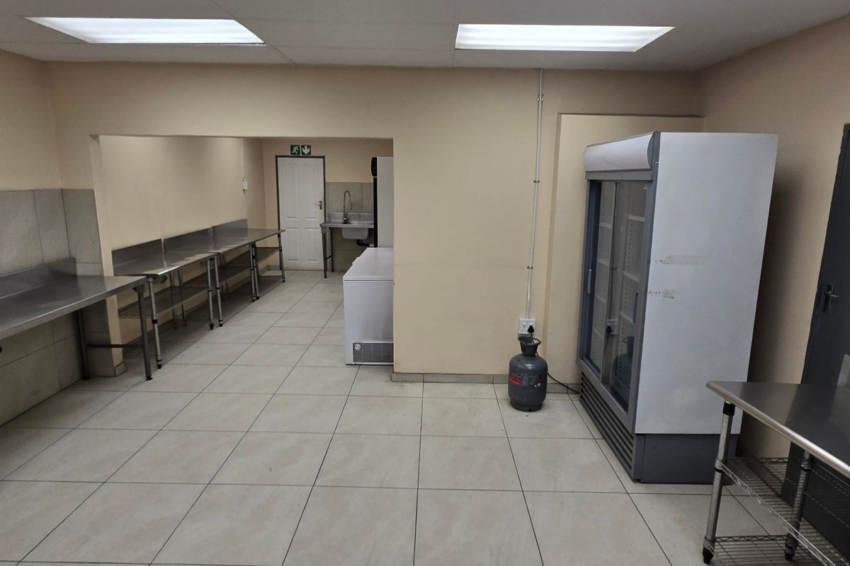A functional industrial kitchen space featuring stainless steel prep surfaces, tiled flooring, and recessed lighting, suitable for commercial food preparation or utility use.