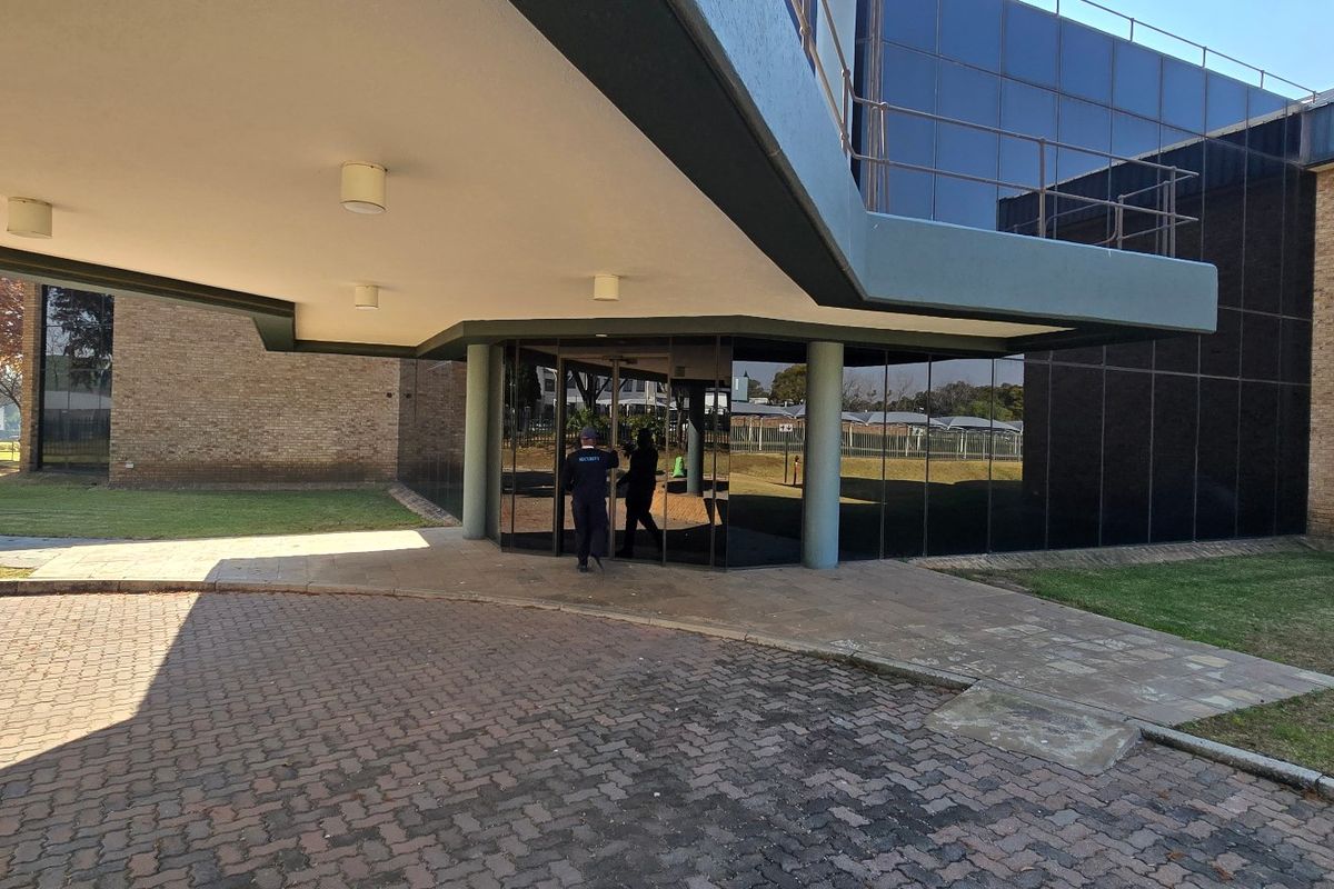 Front entrance of an industrial building featuring a covered canopy, brick facade, and modern glass curtain walling with a paved driveway.