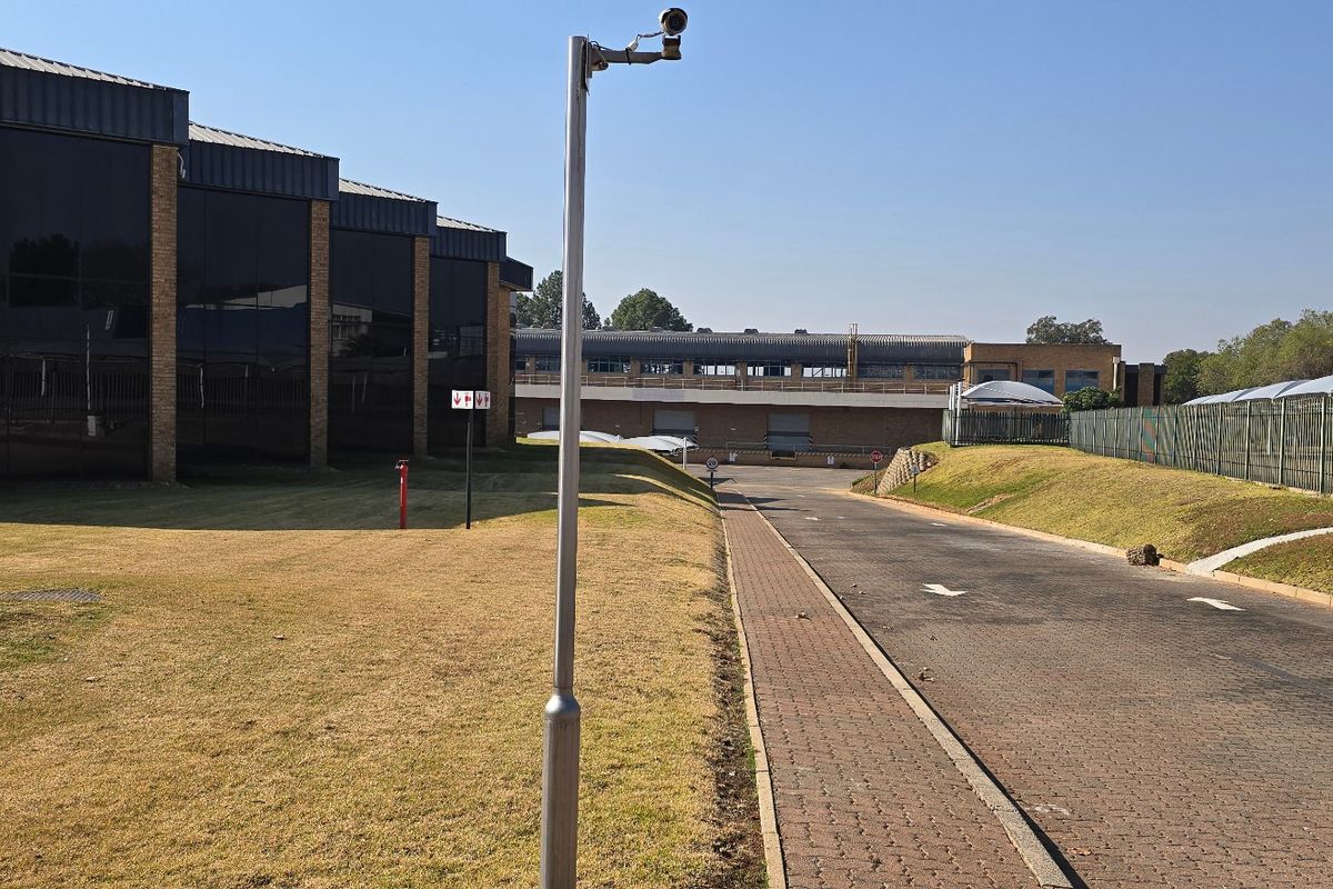 Exterior view of an industrial property featuring a paved driveway, brick facade with tinted windows, and secure perimeter fencing.