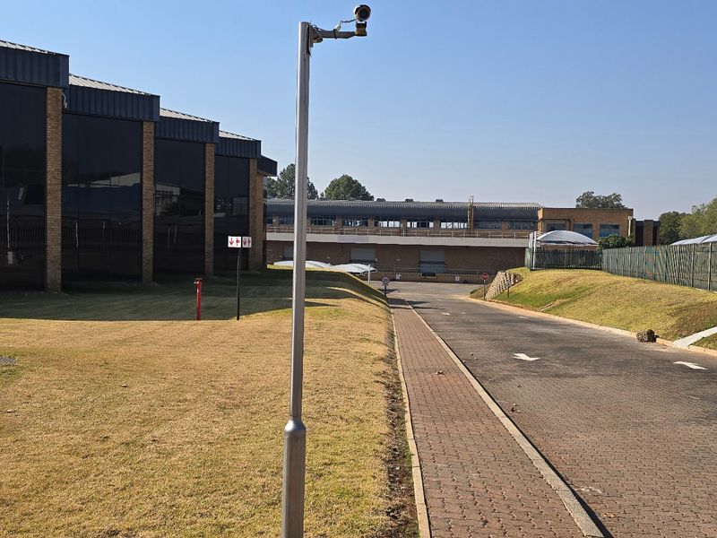 Exterior view of an industrial property featuring a paved driveway, brick facade with tinted windows, and secure perimeter fencing.