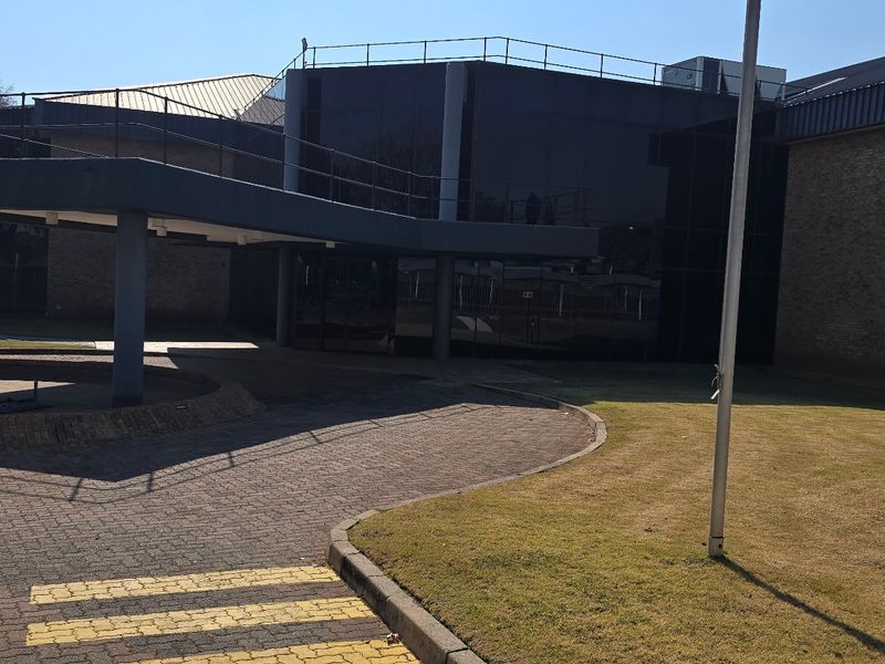 Front exterior view of a commercial industrial building featuring a covered entrance canopy, dark glass curtain walling, and paved driveway access.