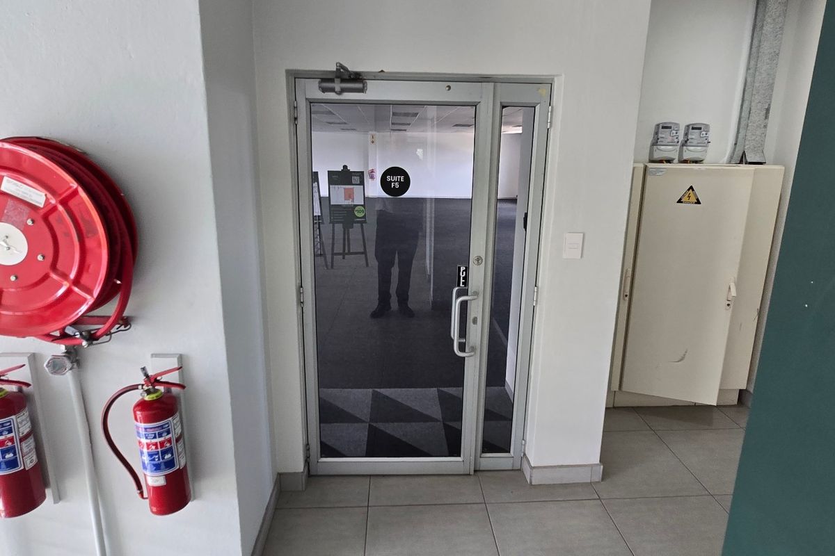 Commercial office suite entrance featuring a glass door, fire safety equipment, and an integrated electrical distribution board in a clean, tiled hallway.