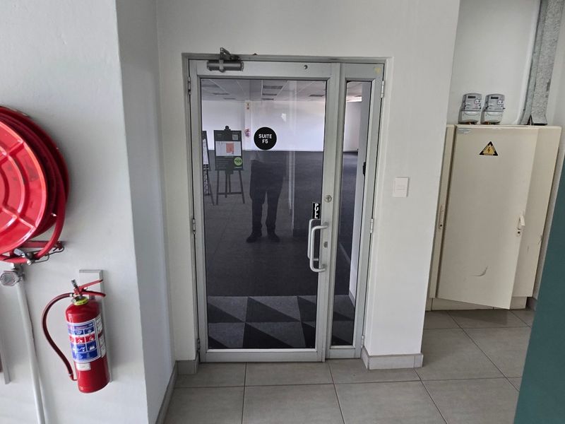 Commercial office suite entrance featuring a glass door, fire safety equipment, and an integrated electrical distribution board in a clean, tiled hallway.