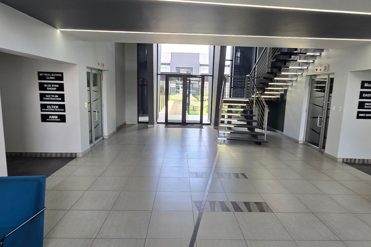 Modern commercial building entrance lobby featuring tiled flooring, a contemporary staircase, and clear directory signage for multiple tenants.