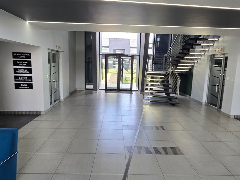Modern commercial building entrance lobby featuring tiled flooring, a contemporary staircase, and clear directory signage for multiple tenants.