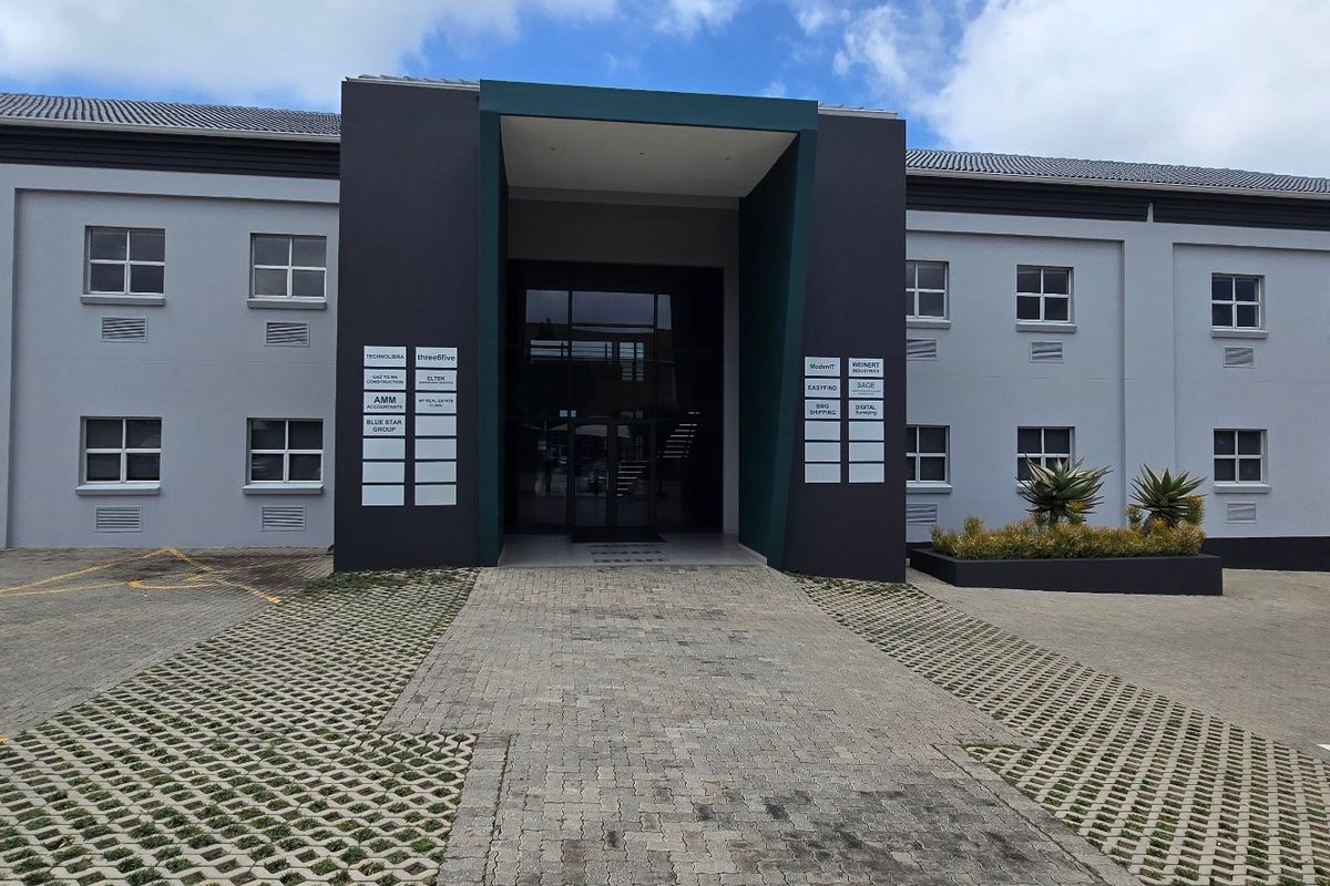 Front facade of a modern commercial office building featuring a paved entrance, glass doors, and professional signage for multiple tenants.