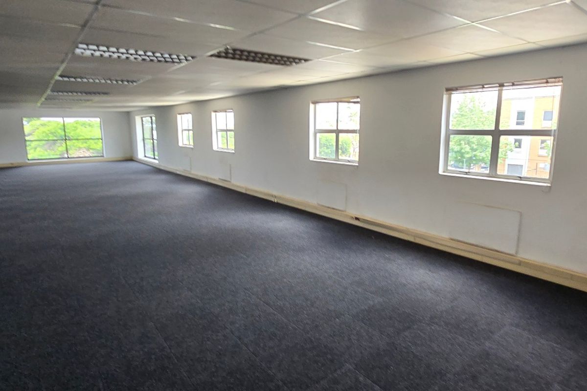 A spacious, open-plan commercial office area featuring a suspended ceiling, recessed lighting, and large windows providing ample natural light.