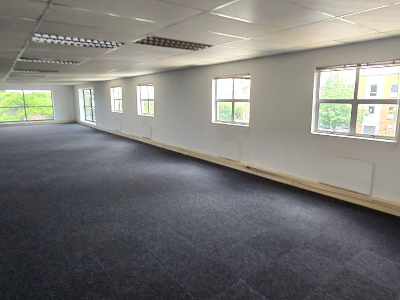 A spacious, open-plan commercial office area featuring a suspended ceiling, recessed lighting, and large windows providing ample natural light.