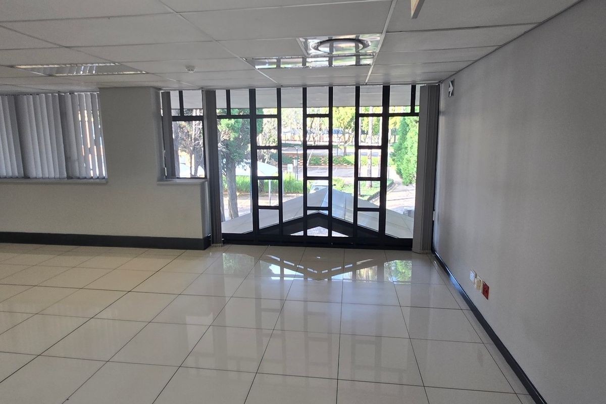 Spacious, empty commercial office area featuring polished tiled flooring, a suspended ceiling with recessed lighting, and large windows with vertical blinds.