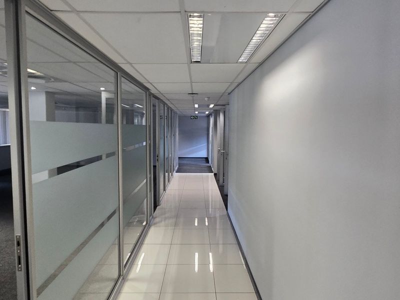 A clean, modern commercial hallway featuring polished tiled flooring, suspended ceilings with recessed lighting, and glass partition walls creating a professional office environment.