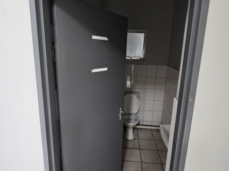 A small, functional bathroom featuring tiled flooring and wall cladding, currently in need of cosmetic updates and maintenance.