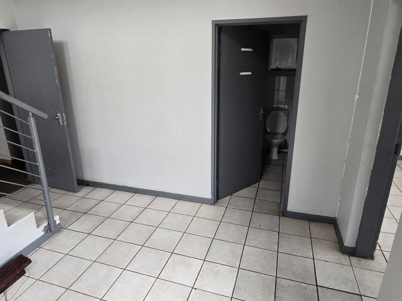 A functional commercial hallway featuring tiled flooring, a staircase with metal railing, and access to an adjacent restroom facility.