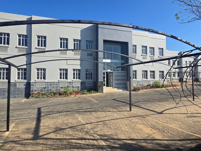 Front exterior view of a multi-story industrial building featuring a paved parking area with metal carport structures and a modern glass entrance.
