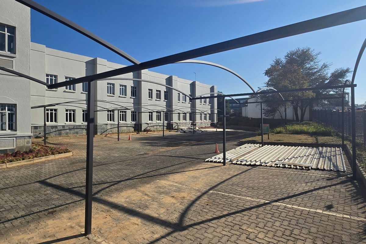 Exterior view of an industrial property featuring a paved parking area with a metal carport structure and a multi-story building facade.