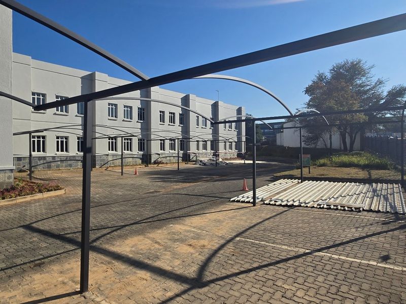 Exterior view of an industrial property featuring a paved parking area with a metal carport structure and a multi-story building facade.