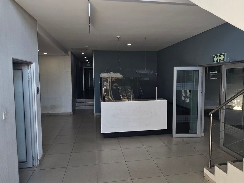 Spacious industrial entry foyer featuring a built-in reception desk, tiled flooring, and a staircase with modern stainless steel railings.