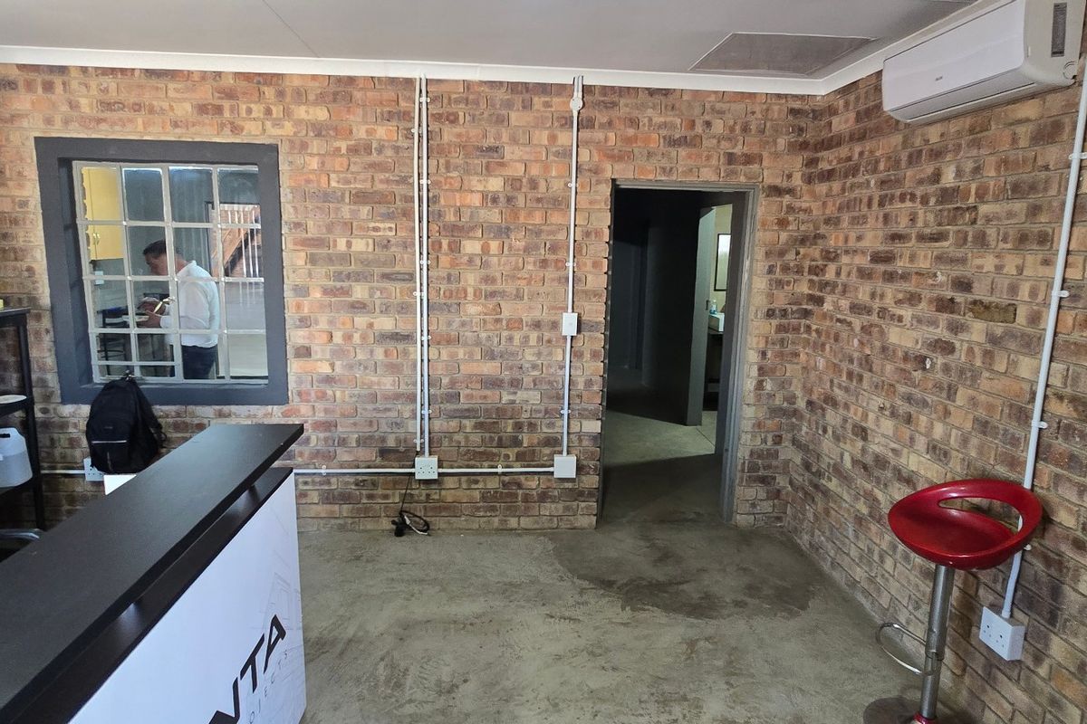 Industrial-style office space featuring exposed brick walls, concrete flooring, and surface-mounted electrical conduits, providing a functional and raw aesthetic.