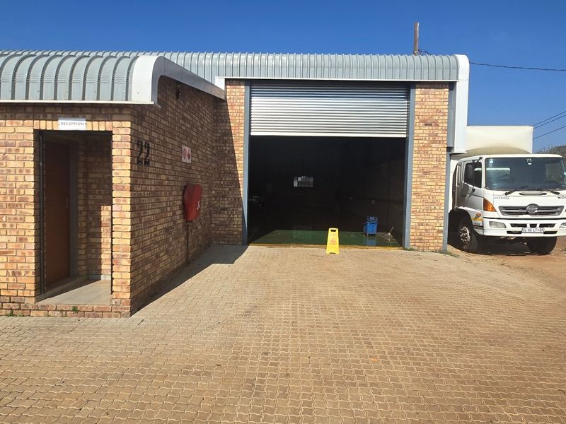 Front view of an industrial property featuring a face brick facade, a large roller shutter door, and a paved driveway area.