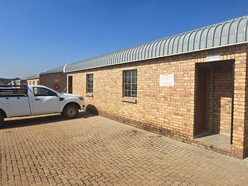 Industrial property exterior featuring a face brick facade, curved metal roofing, and a paved driveway area with a designated reception entrance.